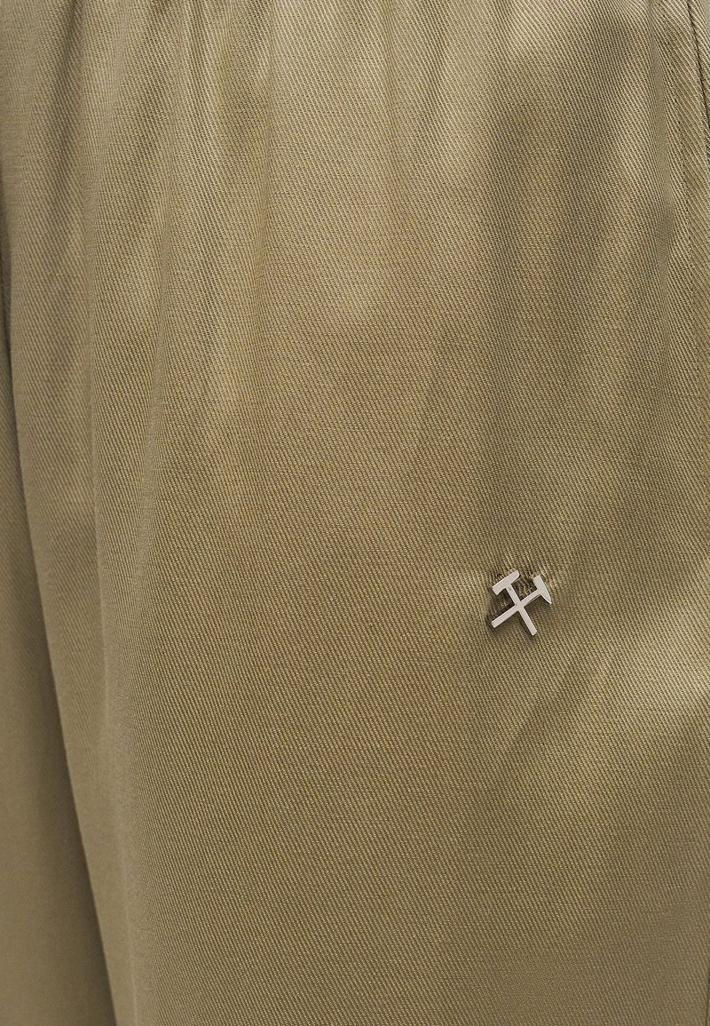 Gros plan sur un tissu beige avec une petite épingle argentée en forme de marteaux croisés attachée près du coin inférieur droit.