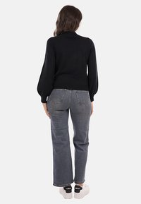 Maglione nero con maniche a palloncino, aderente in vita, abbinato a jeans grigi a gamba dritta a vita alta e sneakers bianche con dettagli neri.