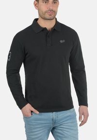 Svart langermet polo skjorte med krage, med brodert logo på brystet og nummer 3 på ermet. Avslappet passform og bomullsstruktur.