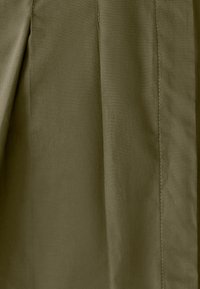 Tessuto verde oliva, con una superficie liscia e cuciture visibili e dettagli a pieghe, che creano un design strutturato.