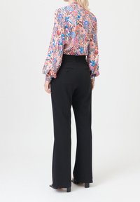 Blouse à motif floral avec manches longues et col montant, associée à un pantalon noir taille haute avec poches arrière.