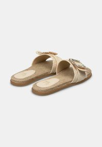 Flat slide sandals in a light gold color with a textured strap featuring a decorative buckle. Cushioned footbed with a natural fiber design.