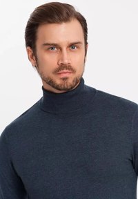 Tmavě modrý rolák vyrobený z měkké, strukturované látky. Přiléhavý střih s vysokým krkem a dlouhými rukávy. Hladký povrch bez vzorů.