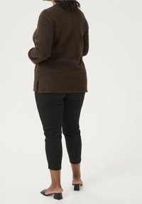 Bruine wollen trui met een ronde hals, zijslitsen en een ontspannen pasvorm, gecombineerd met zwarte aansluitende broek en blokhak instappers.