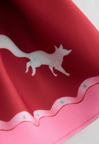 Czerwono-różowy szalik z białym sylwetką lisa. Brzegi zdobione są falistym wzorem z małymi niebieskimi akcentami. Wykonany z gładkiej tkaniny.