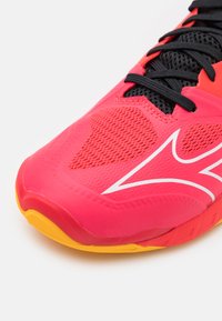 Bright pink athletic shoe with a textured surface, mesh detailing, black laces, and a yellow outsole. Features a white logo design.