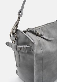 Borsa a mano in pelle grigia con una forma strutturata, caratterizzata da una chiusura superiore con zip, ferrature in metallo e accenti cuciti. Tracolla regolabile attaccata.