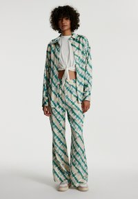 Zweiteiliges Outfit bestehend aus einem langärmeligen Shirt mit Batikmuster in Creme und Teal sowie passenden weit geschnittenen Hosen, die aus leichtem Stoff gefertigt sind.