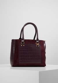 BurGundy håndtaske med krokodilleprægning, suede accenter, guldfarvet hardware og to håndtag; rektangulær form med en struktureret design.