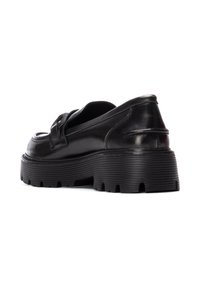 Mocasines de cuero negro con una suela gruesa y estriada. Presentan una punta redonda y una correa decorativa en la parte superior. Textura suave y diseño elegante.