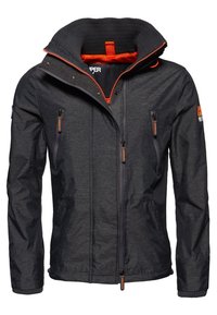 Chaqueta de color gris oscuro con un alto cuello, con acentos naranjas, múltiples bolsillos con cremallera y puños acanalados para mayor textura. Material duradero.