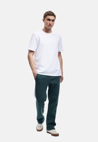Hvid bomulds T-shirt parret med mørkegrønne sweatpants. Outfittet komplementeres af hvide sneakers med brune såler. Enkel, afslappet design.