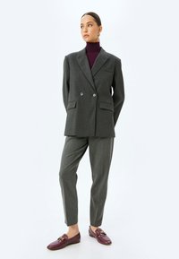 Dark gray double-breasted blazer with two front pockets, paired with tapered gray trousers and burgundy loafers featuring a gold accent.
