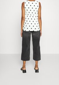 Ljust grön ärmlös blus med svarta prickar, cinchad midja, ihop med lösa svarta cropped jeans och svarta klacksandaler.