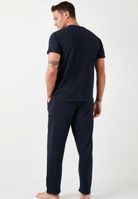 Pijamas azul marino hechos de una tela suave; la camiseta presenta un cuello crew, corte holgado; los pantalones tienen bolsillos laterales y un diseño de pierna entallada.