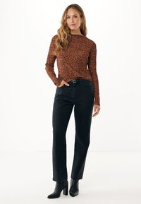 Braun geflecktes Langarmoberteil, kombiniert mit hochtaillierten schwarzen Jeans im geraden Schnitt und schwarzen, Absatz-Ankle-Boots. Schlichter weißer Hintergrund.