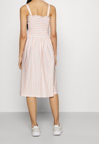 Lätt midi-klänning med rosa och vita ränder, texturerad smockad bodice, volangkanter på banden och en svävande kjol. Matchad med vita sneakers.