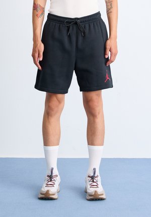 Shorts de sport noirs avec une taille élastique et un cordon de serrage, ornés d'un logo Jumpman rouge, associés à des chaussettes blanches et des baskets multicolores.