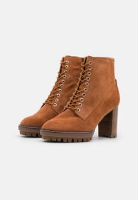 Stivaletti in suede marrone con tacco alto e impilato, lacci sul davanti e punta rotonda. Presentano occhielli in metallo e una suola robusta per una migliore aderenza.