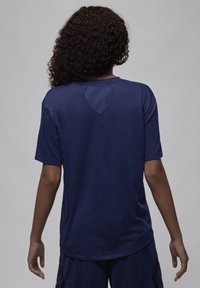 T-shirt de algodão azul-marinho com mangas curtas, decote arredondado e um detalhe em formato de diamante nas costas. Textura suave, ajuste casual.