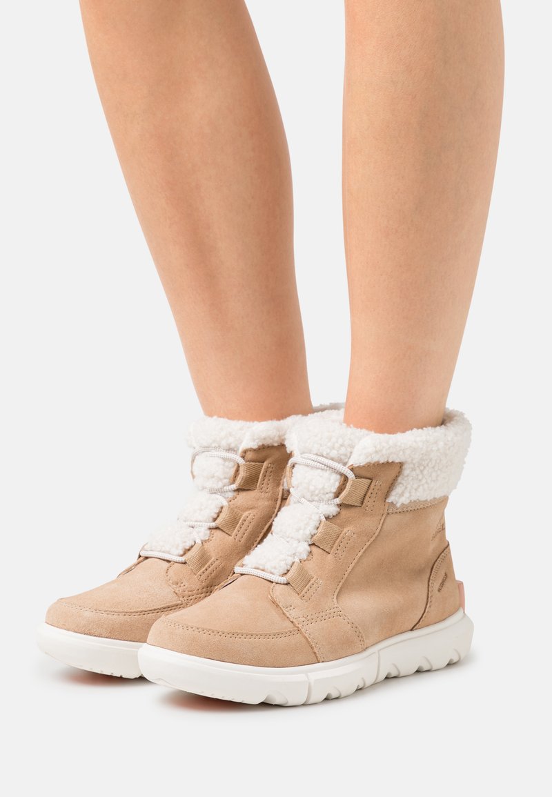 Bottines en suède beige avec un col en fourrure blanche, dotées de lacets gris et d'une semelle en caoutchouc texturée avec une légère touche de rose.
