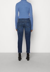 Suéter azul de punto trenzado, metido dentro de unos jeans de mezclilla azul oscuro. Los jeans tienen un corte recto, con dos bolsillos traseros y un ligero desgaste en los muslos.