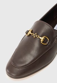 Pruun nahkne loafer sileda tekstuuriga, millel on kuldse tooni ketikäik ja ümar varvasemuster.