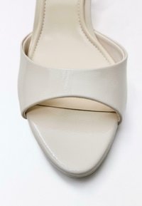 Sandale à bout ouvert en cuir verni beige avec une large bride sur le devant et une semelle intérieure légèrement rembourrée.