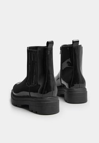 Stivaletti alla caviglia in pelle patinata nera con pannelli laterali elastici, suola nera spessa e linguette posteriori per una facile calzata; presentano una chiusura con zip.