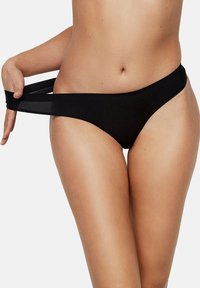 Vrouw in zwarte bikini-broekjes die de tailleband van de heup trekt om de rek en pasvorm tegen de huid te laten zien.