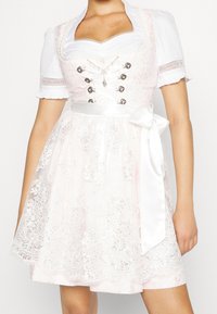 Robe dirndl rose avec un corsage en dentelle, des manches courtes blanches, des boutons décoratifs, une ceinture en ruban satinée et une broderie complexe à l'ourlet.