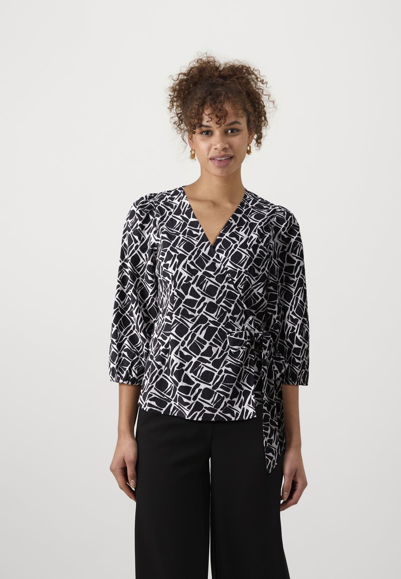 Blouse enroulée à motifs noir et blanc avec des manches trois-quarts, un décolleté en V et un nœud à la taille. Texture de tissu lisse.