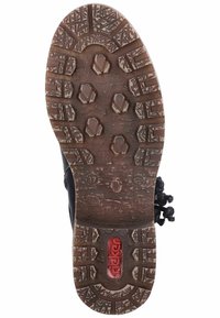 Semelle de chaussure noire avec des crampons en caoutchouc proéminents, des motifs texturés et un logo rouge. Comprend des éléments de grip circulaires et hexagonaux.