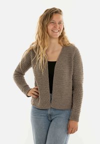 Grijze gehaakte cardigan met een open voorkant, gestructureerd oppervlak en ribgebreide mouwen, gecombineerd met high-waisted jeans en een zwart topje.