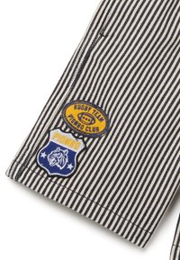 Tessuto a righe con toppe ricamate blu e gialle. Le toppe includono "Rugby Team Piombo Club" e un emblema di leone blu con "Piombo."