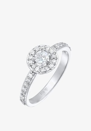 Sølv ring med en rund, central klar ædelsten omgivet af mindre klare sten. Glat bånd med subtile teksturerede detaljer.