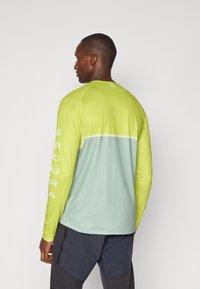 Langærmet atletisk skjorte i lys limegrøn og blød blå gradient. Har ergonomisk design, kontrasterende ærmer og logo på ryggen.