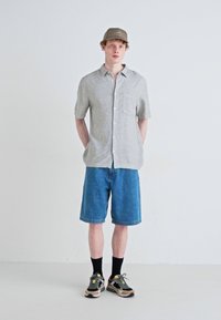 Lys grå kortermet skjorte med lomme, blå denimshorts, svarte sokker og flerfargede joggesko, toppet med en beige caps.