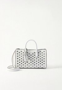 Hvit Michael Kors-veske med svarte runde nagler, doble håndtak og avtakbar skulderrem på hvit bakgrunn.