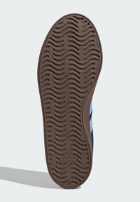 Brun gummisula med vågig mönster, med ljusblå och marinblå ränder på sidan. Texturerad för grepp och dragkraft.