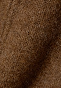 Gros plan sur un tissu tricoté doux et marron montrant la texture détaillée et les fibres du matériau.