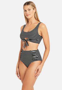 Bikini a righe bianche e nere, con top corto dettagliato da un nodo frontale e slip a vita alta con lati arricciati. Texture liscia.