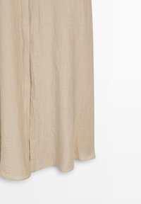 Beiger Leinenstoffvorhang, der gerade hängt, mit subtiler Textur und weichen Falten, vor einem weißen Hintergrund.