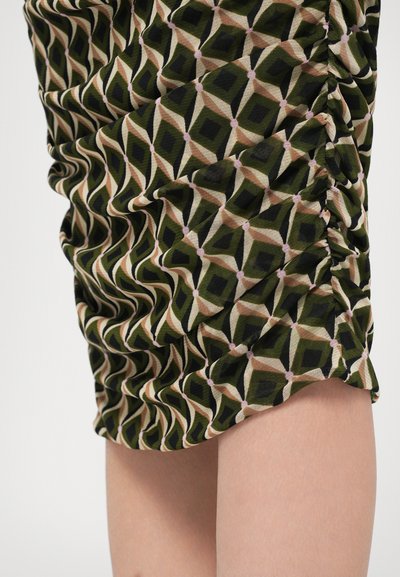 Mini spódnica z marszczeniami w zielono-czarnym, beżowym i różowym geometrycznym wzorze w diamenty noszona na nagiej udzie.