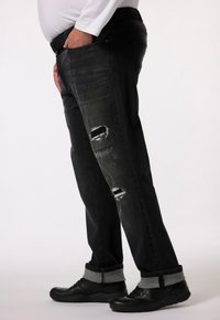 Jeans de mezclilla negros con detalles rasgados en los muslos, corte recto, puños enrollados y combinados con zapatillas deportivas negras.