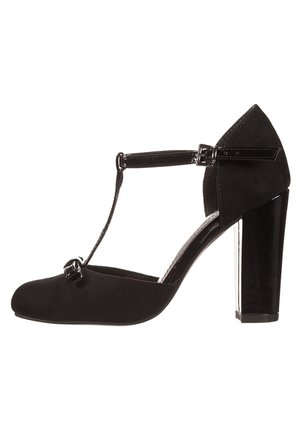 Black T-strap high heel shoe with a suede upper, patent leather accents, wide block heel, and smooth rounded toe. Features a buckle closure.