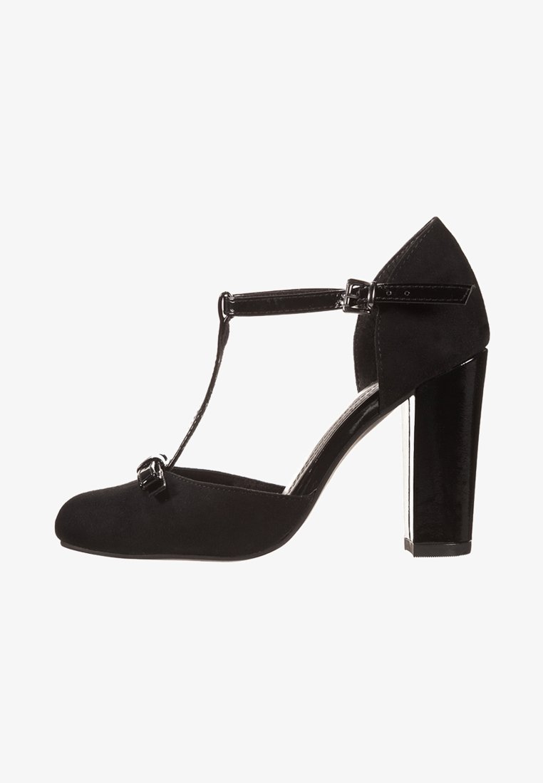 Chaussure à talon haut noire en T avec une tige en daim, des accents en cuir verni, un large talon bloc et un bout arrondi lisse. Présente une fermeture à boucle.