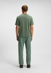 Grøn kortærmet skjorte med lige snit, parret med grønne mønstrede joggingbukser. Sorte sneakers fuldender outfittet.