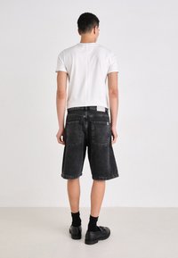 Schwarze Denim-Shorts mit lockerer Passform, umgeschlagenem Saum und zwei Gesäßtaschen. Kombiniert mit einem schlichten weißen T-Shirt mit kurzen Ärmeln und schwarzen Schuhen.