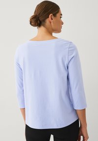 Lichtpaarse langemouwen top met een brede halslijn en 3/4 mouwen. Zacht katoenmateriaal, naadloze achterkant en een relaxed fit.